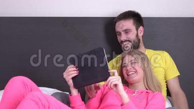 微笑的情侣在床上看平板电脑上的电影